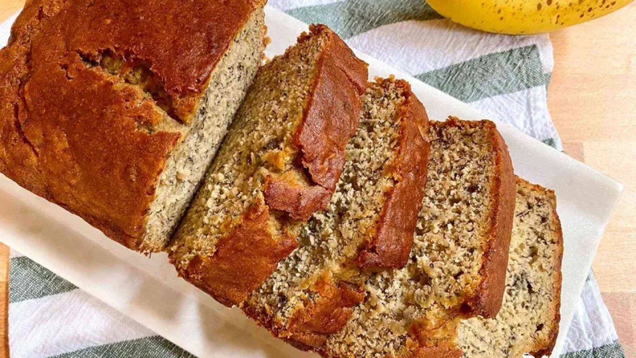 Sepotong roti pisang panggang yang lembut, disajikan dengan potongan pisang segar dan taburan kacang almond